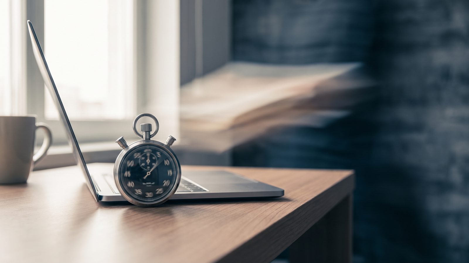 A stopwatch on a clean desk beside a laptop in soft light