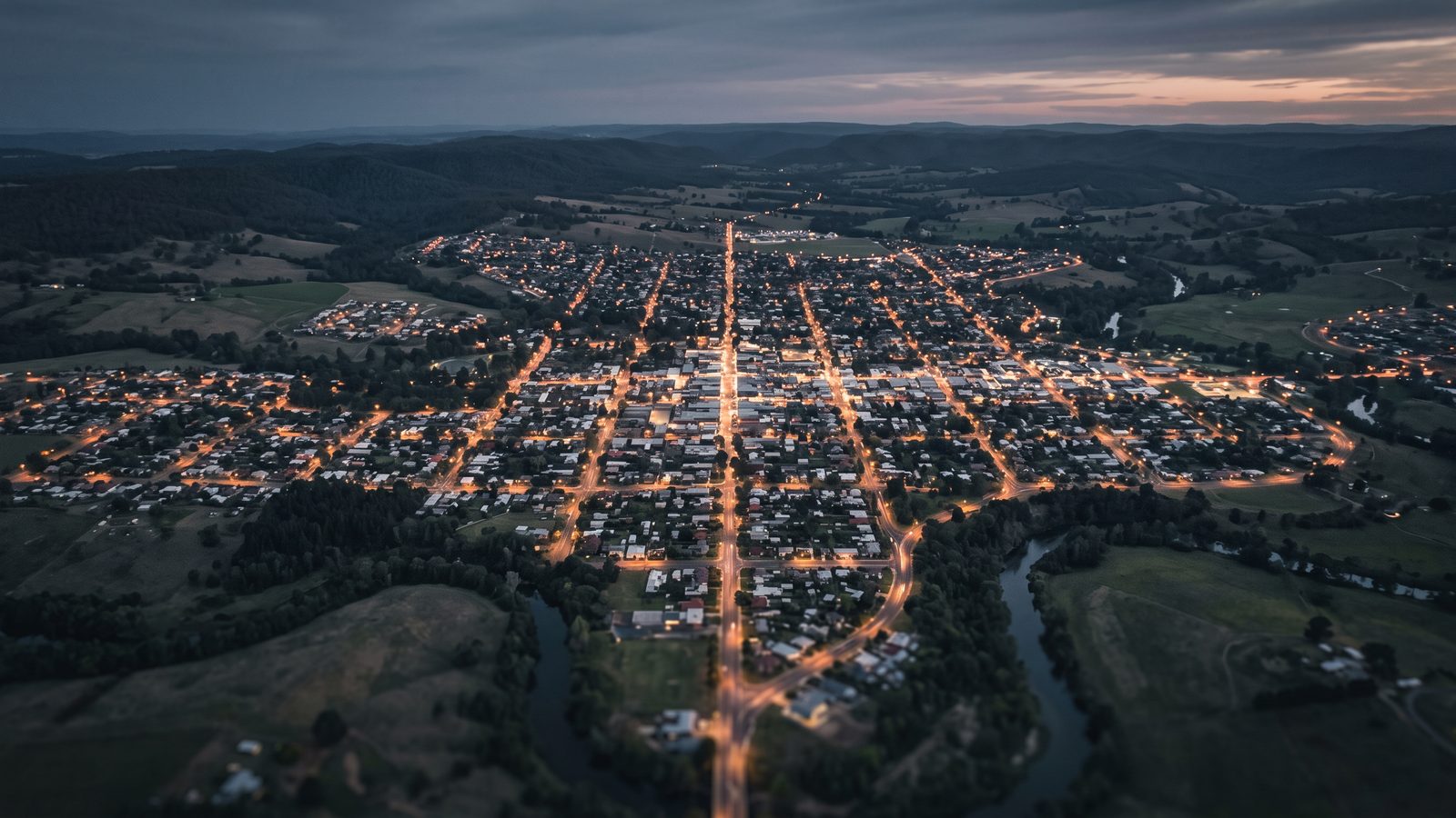 An aerial dusk view of a town grid with warm streetlights